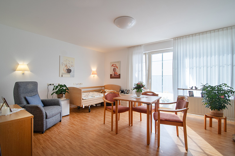 Bewohnerzimmer mit Bett, Sitzecke und bodentiefen Fenstern