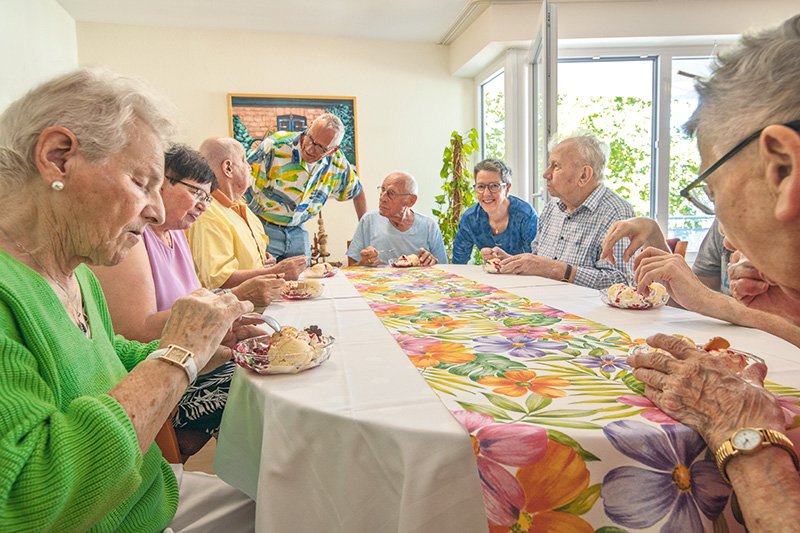 Bewohnergruppe und Pflegekräfte essen Eis im Wohnzimmer