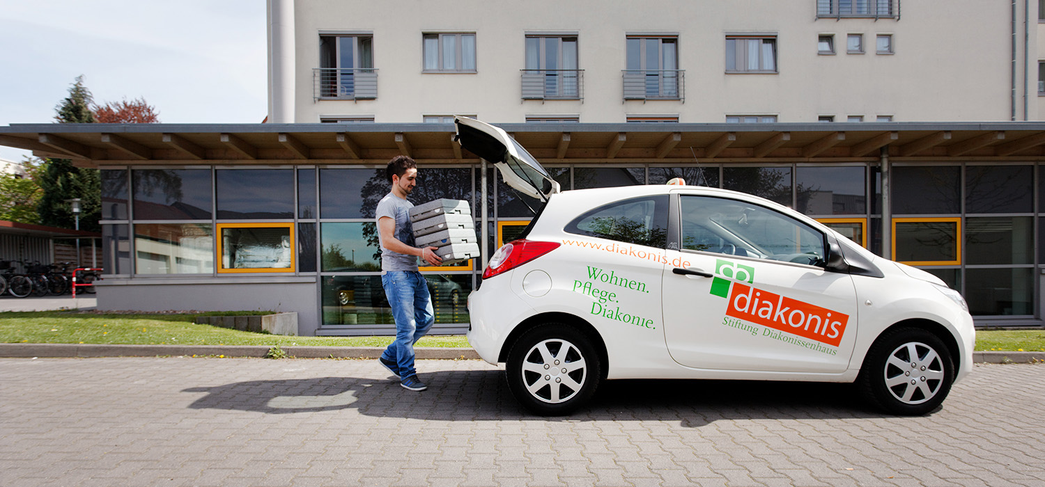diakonis-Fahrzeug wir vom Auslieferungsfahrer mit Essens-Containern beladen