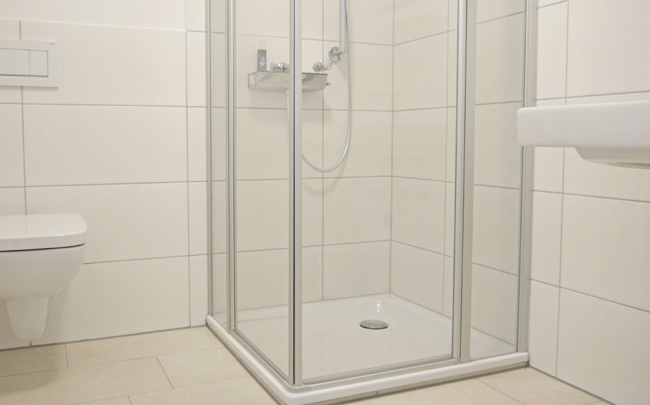 Ein WC und eine fast ebenerdige Dusche in einem weiß gefliesten Badezimmer