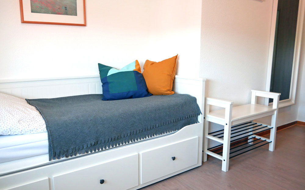 Ein weißes Bett mit grauer Decke und einem blauen und einem gelben Kissen darauf