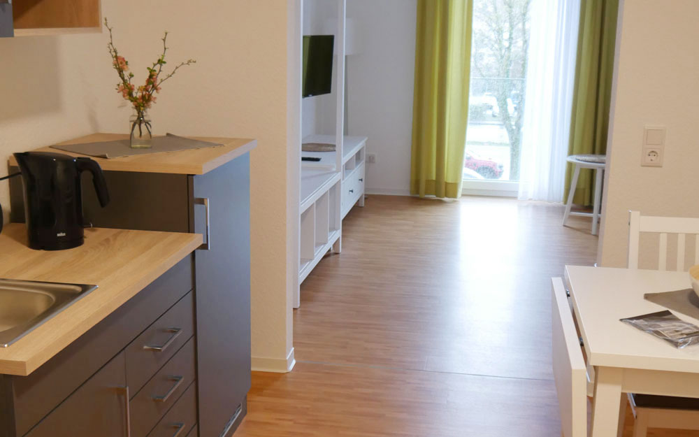 Blick in ein Zimmer mit kleiner Küchenzeile links und einem kleinen Esstisch rechts