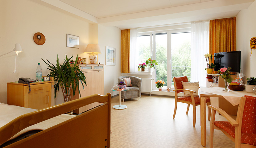 Bewohnerzimmer mit Bett, Sitzecke und bodentiefen Fenstern