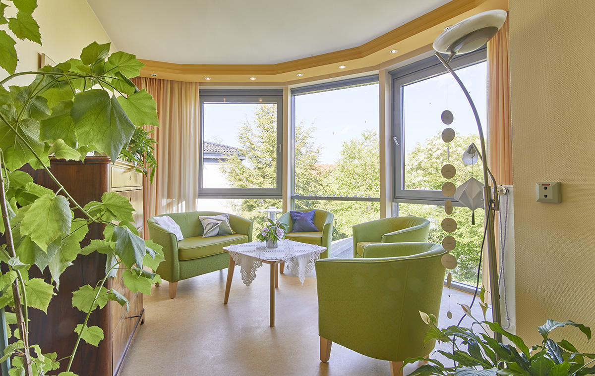 Sitzecke mit grüner Polstergarnitur, bodentiefen Fenstern und Blick in den Garten