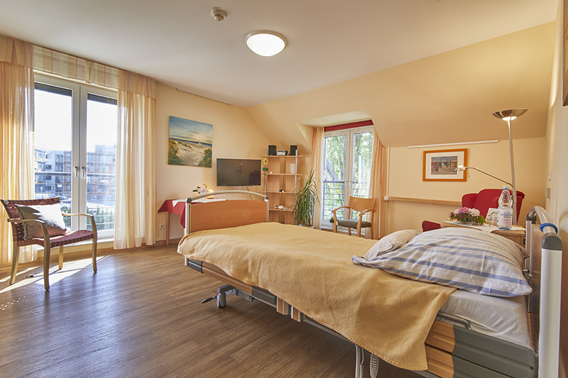 Gastzimmer mit Krankenbett, Sessel, bodentiefen Fenstern und Blick auf das Klinikum Detmold