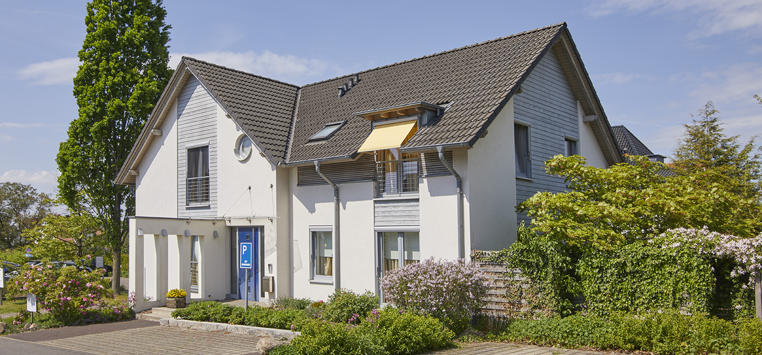 Außenansicht Hospiz, umgeben von Bäumen mit vorgelagerten Parkplätzen