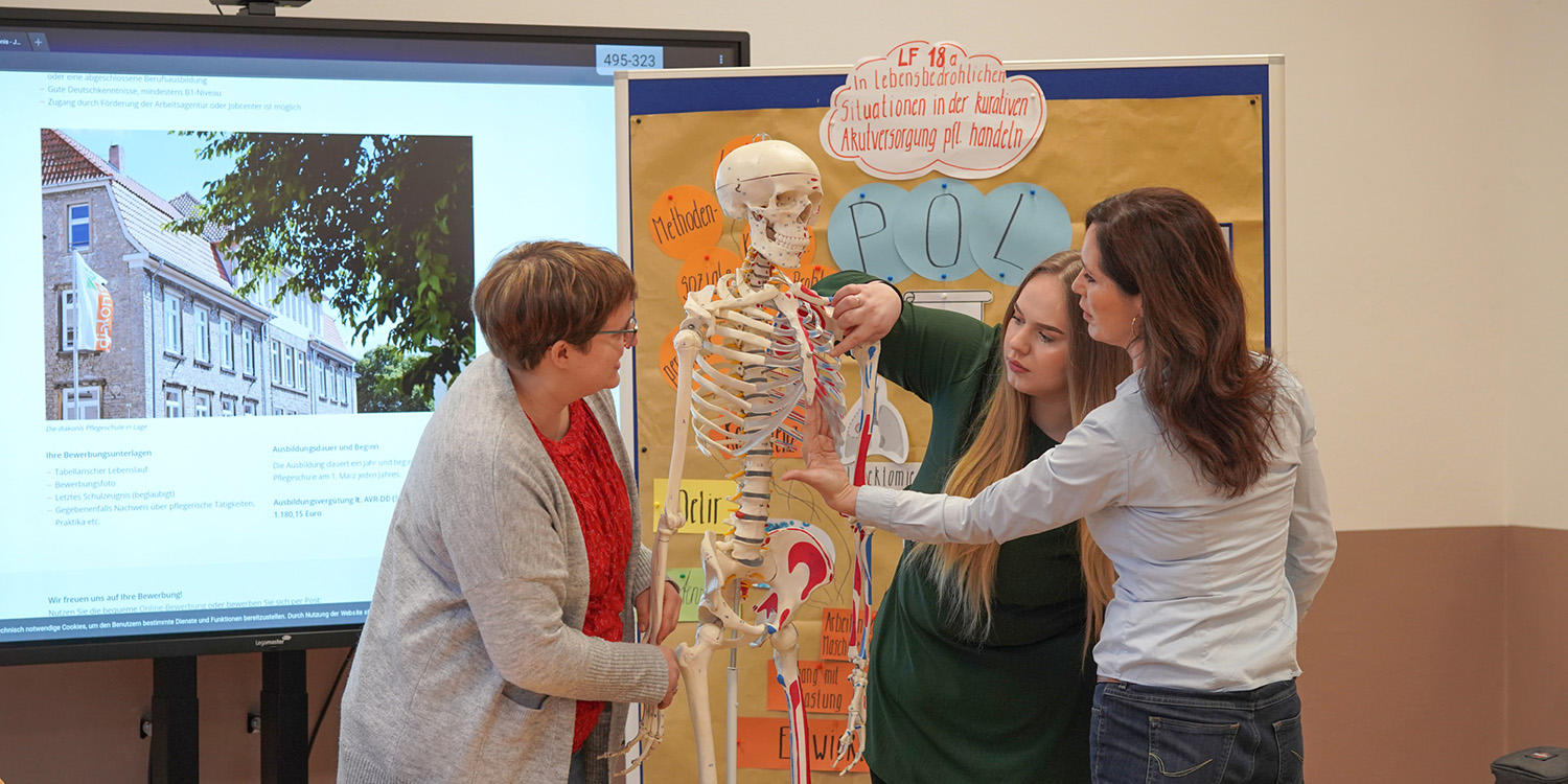 Praktischer Unterricht an einem Skelett mit Lehrerin und zwei Schülerinnen