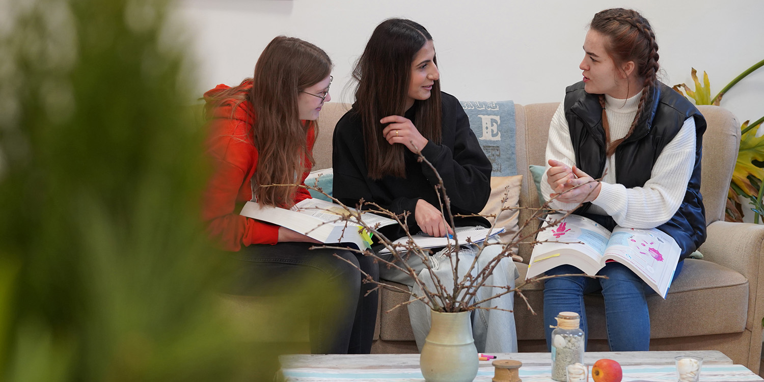 Drei Pflegeschülerinnen lernen auf einem Sofa mit Lehrbüchern