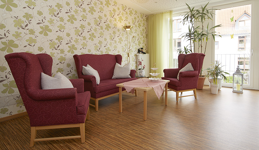 Wohnzimmer im Seniorenzentrum mit gemütlicher Polstergarnitur und Blick aus den großen Fenstern