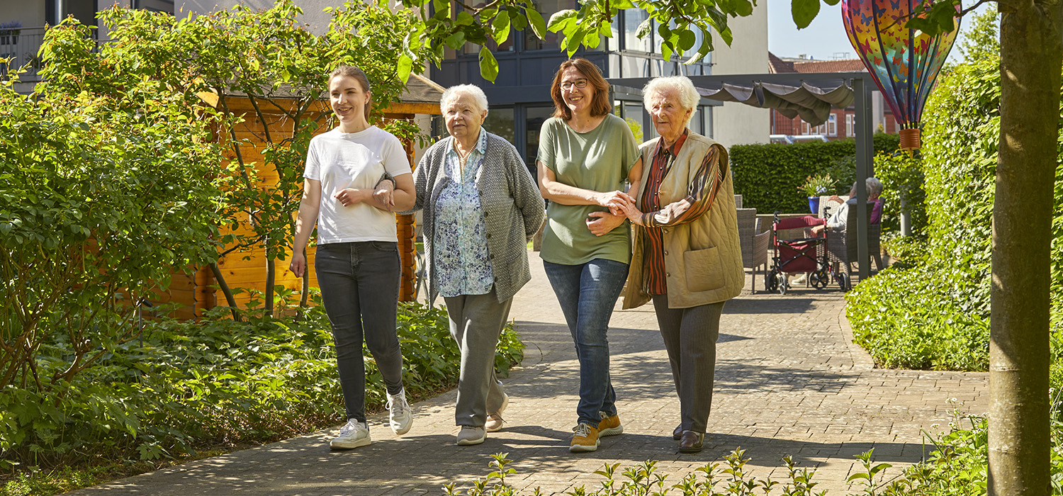 Zwei Pflegekräfte machen einen Spaziergang mit zwei Bewohnerinnen im Garten der Tagespflege Detmold