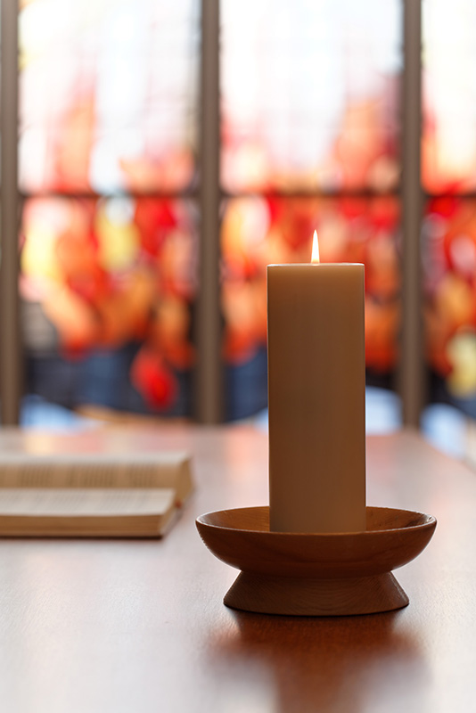 Brennende Kerz auf einem Altar vor Kirchenfenster