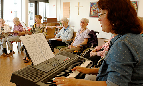 Mitarbeiterin spielt Keybord für eine Gruppe von Bewohnern