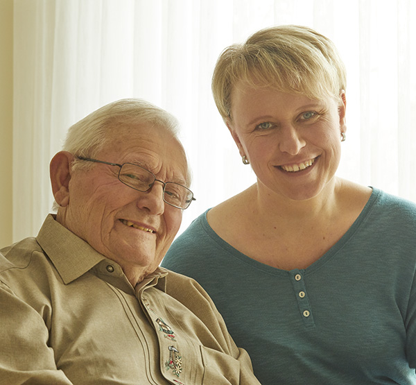 Pflegekraft und alter Herr schauen lachend in die Kamera