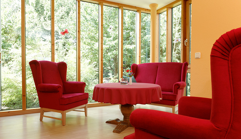 Sitzbereich mit Sesseln, Sofa und großen Holzfenstern mit Blick ins Grüne