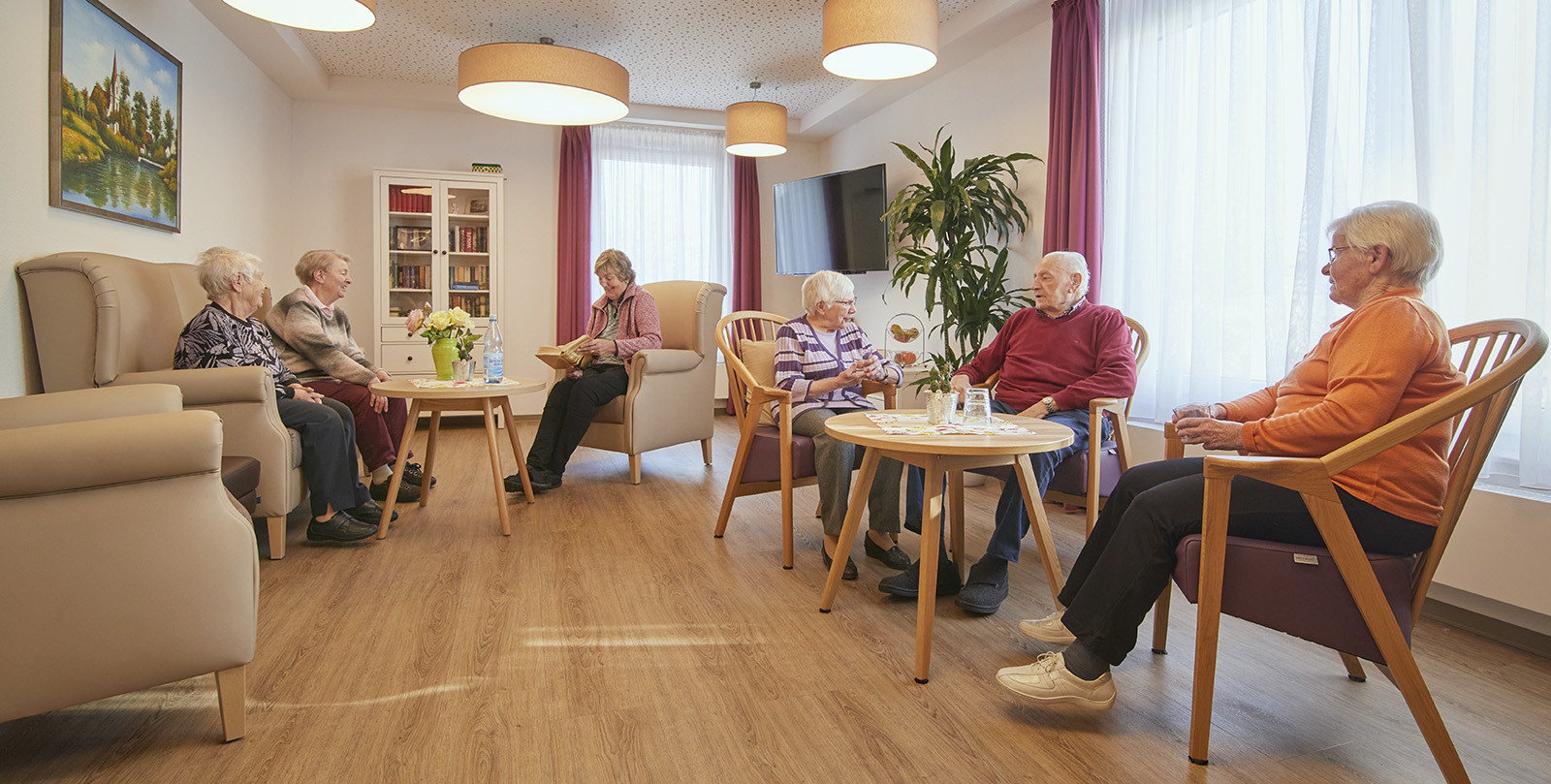 Wohnzimmer mit Bewohnern auf Sesseln und Sofa