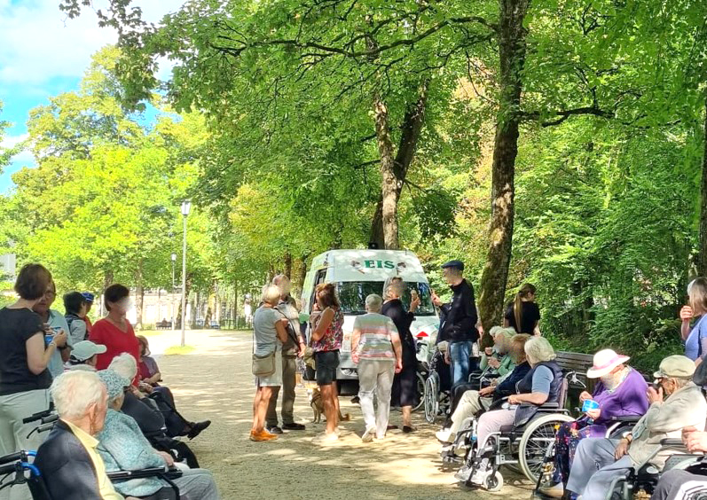 Die Gruppe sitzt am Wegesrand und isst Eis. Der Eiswagen steht im Hintergrund.